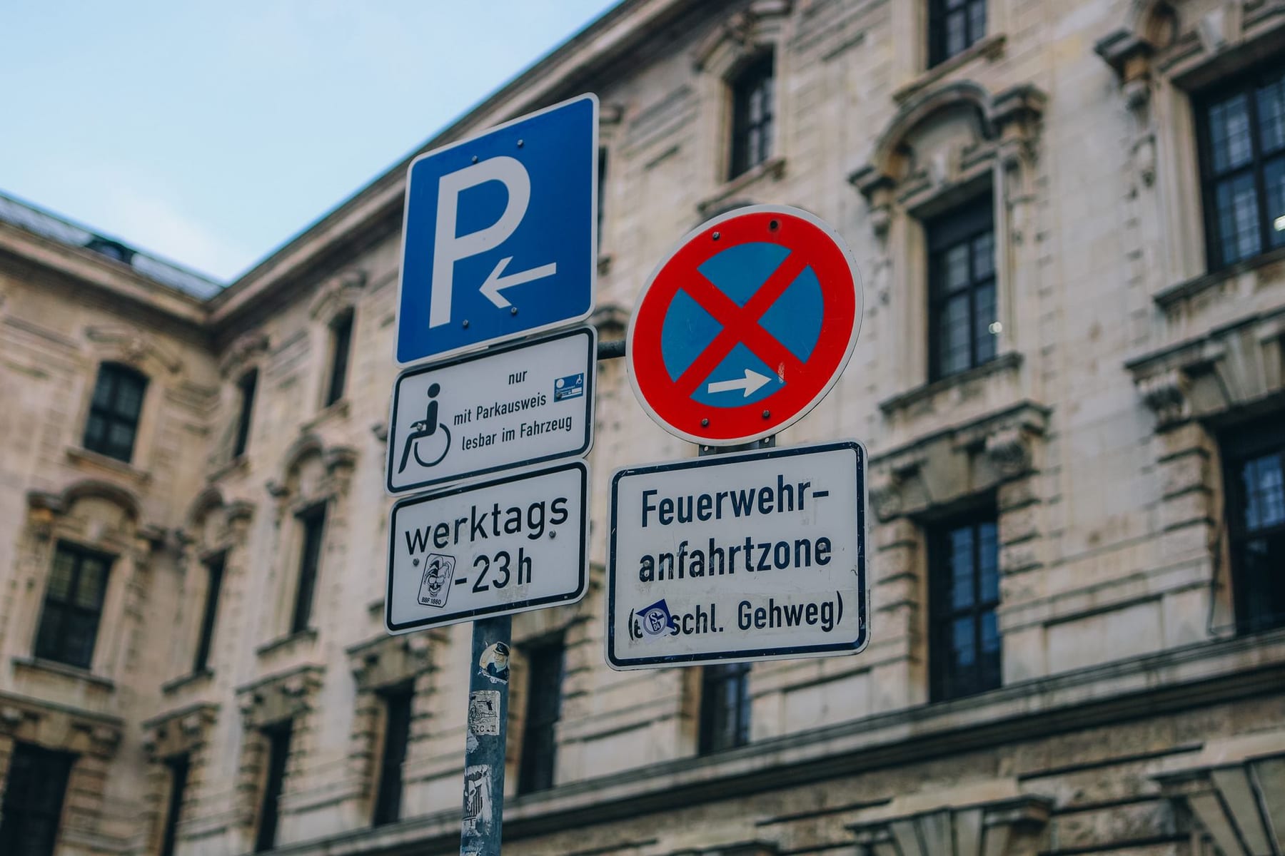 German street signs in front of an old stone building; one of them reads Feuerwehranfahrtzone.