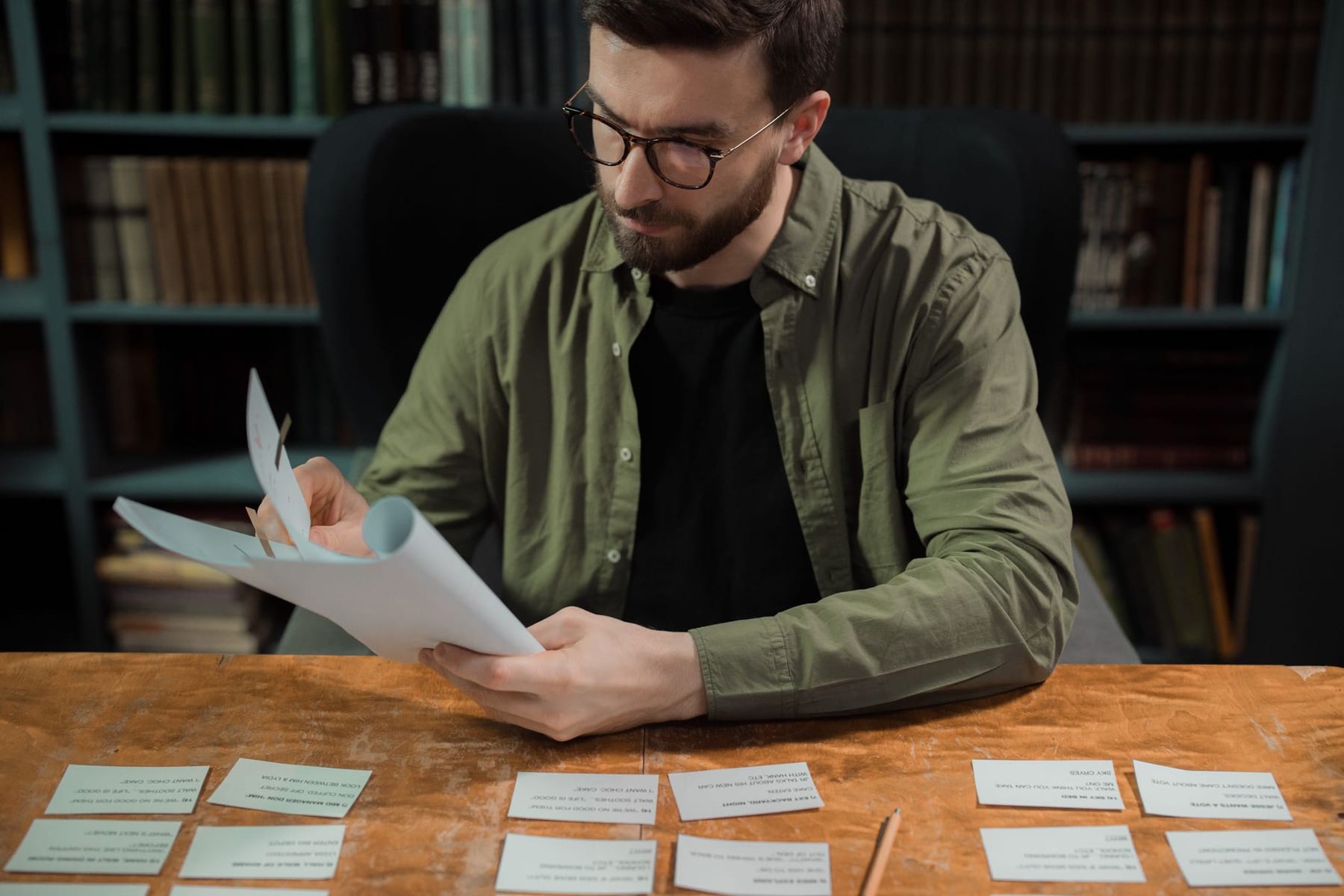 A man at a desk reading through his notes, with rows of small printed cards laid out in front of him.