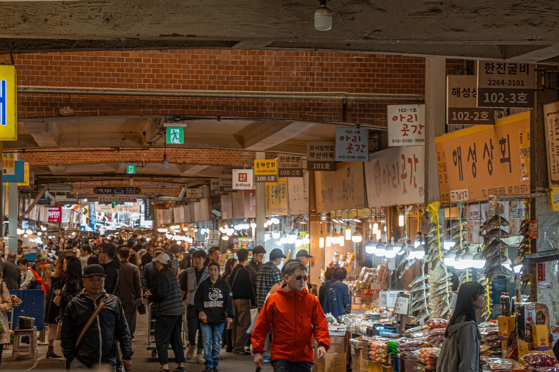 A busy covered market in Korea, with shop signs in Hangul hanging above the stalls.